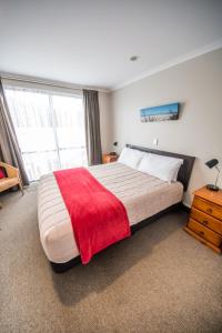 a bedroom with a large bed with a red blanket on it at Bay Palm Motel in Mount Maunganui