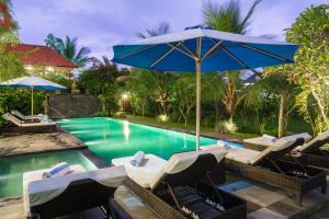 a pool with chairs and an umbrella next to a swimming pool at Kiskenda Cottages & Restaurant in Ubud