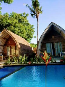 a house with a thatch roof next to a swimming pool at Gili Matiki in Gili Islands