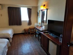Habitación de hotel con escritorio, TV y cama en Little Paradise Inn, en Hengchun