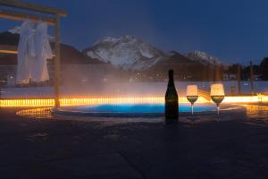a bottle of wine and two glasses next to a pool at Mountainlodge Luxalpine in San Vigilio Di Marebbe