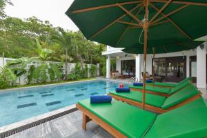 a swimming pool with a green umbrella and lounge chairs at An Bang Beach Villa in Hoi An