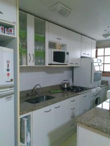 a kitchen with white cabinets and a sink and a microwave at Apartamento Centro Gramado in Gramado