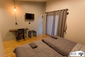 a bedroom with two beds and a desk and a television at Bed Box in Nakhon Ratchasima