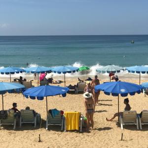 a group of people on a beach with blue umbrellas at KARON SINO House in Karon Beach
