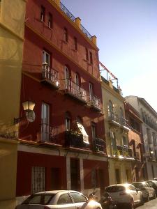 un edificio rojo alto con coches estacionados frente a él en TRIANA PUREZA 1, en Sevilla