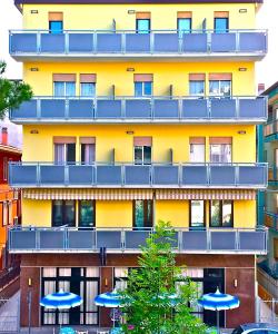 un grand bâtiment jaune avec des parasols bleus devant lui dans l'établissement Hotel Belvedere, à Sottomarina