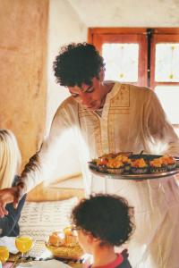 un homme tenant une assiette de nourriture sur une table dans l'établissement Ayouze Auberge, à Aït Ben Haddou