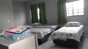 3 camas en una habitación con cortinas verdes en Pousada Agua Quente, en Rio Quente