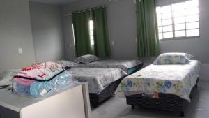 three beds in a room with green curtains at Pousada Agua Quente in Rio Quente