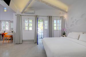 a white bedroom with a large bed and a table at Kouros Village Hotel - Adults Only in Perissa