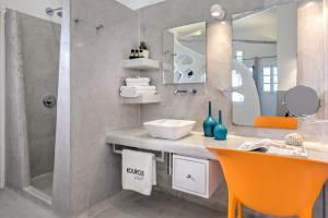 a bathroom with a sink and a mirror and orange chairs at Kouros Village Hotel - Adults Only in Perissa