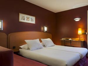 a hotel room with a large bed with white pillows at Sky Hotel Goussainville Charles de Gaulle in Goussainville