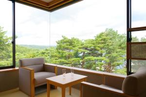 a room with a chair and a table and large windows at Jodogahama Park Hotel in Miyako