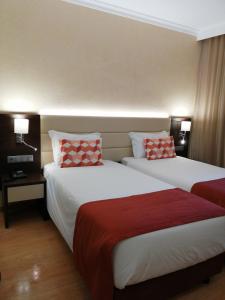 two beds in a hotel room with red and white pillows at Hotel Monaco in Faro