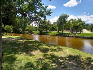 Un río en un parque con un árbol y césped en Las Cuatro Estaciones en Villa Cura Brochero