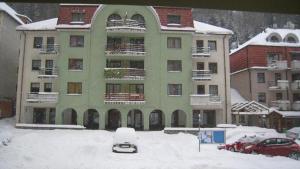 a large green building with cars parked in the snow at Apartman 404 in Jáchymov