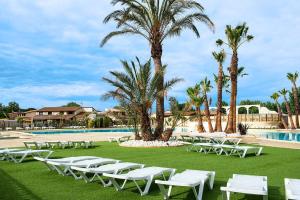 a group of white chairs and palm trees near a pool at Portiragnes-Plage - Les Portes du Soleil - Maison 75m² - A2 in Portiragnes