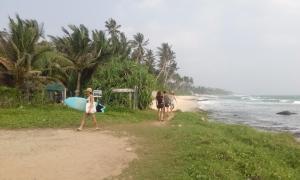 a group of people walking on a beach with a surfboard at Villa Agrico and Surf Guest in Weligama