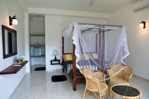 a bedroom with a bed with a canopy and chairs at Villa Kaya Guest House in Hikkaduwa