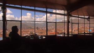 una persona sentada en una mesa mirando por una ventana grande en Hostal Tu Hogar, en Cusco