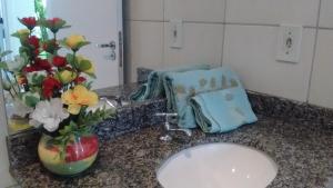 a bathroom counter with a sink and a vase of flowers at Natal RN Apartamento in Parnamirim
