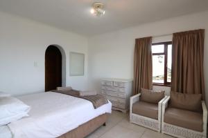 a bedroom with a bed and a chair and a window at Villa Granada in Plettenberg Bay