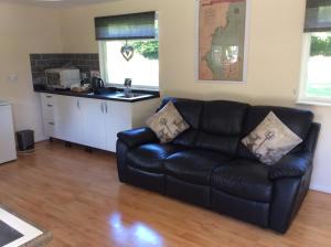 ein Wohnzimmer mit einem schwarzen Sofa und einer Küche in der Unterkunft The Firs in Ashford