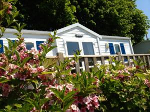 ein weißes Haus hinter einem Zaun mit rosa Blumen in der Unterkunft Camping Le Walric in Saint-Valery-sur-Somme