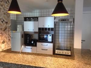 a kitchen with white cabinets and a sink with two lights at Apart Guarapari Residence - Areia Preta in Guarapari