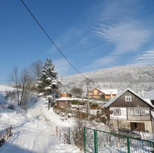 a snow covered village with a house and a fence at Domek nad Potokiem in Słotwiny