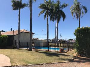 a fence around a swimming pool with palm trees at Wagon Wheel Motel in Cloncurry