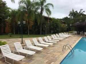 a row of white chairs next to a swimming pool at Recanto da Enseada - Condomínio Via Marina in Ubatuba