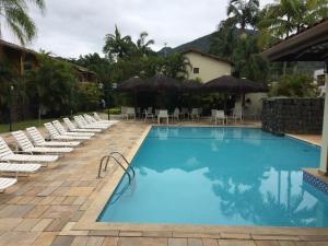 a large swimming pool with chairs and umbrellas at Recanto da Enseada - Condomínio Via Marina in Ubatuba
