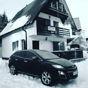 弗拉西克的住宿－Vikend Kuća Iman，一辆停在房子前面雪地里的黑色汽车