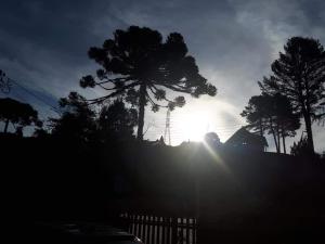 una puesta de sol detrás de los árboles y una valla en A casa Girassol, en Campos do Jordão