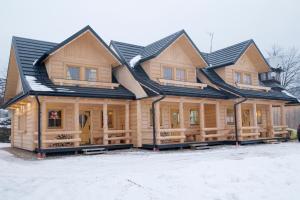 una casa de madera con techo de gambrel en la nieve en Góralskie domki - Kluszkowce en Kluszkowce