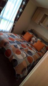 a bed with orange pillows and a comforter in a bedroom at Flamingo land le maple grove caravan hire in Kirby Misperton