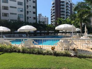 a swimming pool with white umbrellas and chairs next to a building at Flat lindo a 120 metros da praia de Riviera de São Lourenço até 4 pessoas in Bertioga