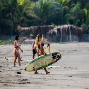 una mujer está sosteniendo una tabla de surf en una playa en Tapas & Surf, en Petacaltepe