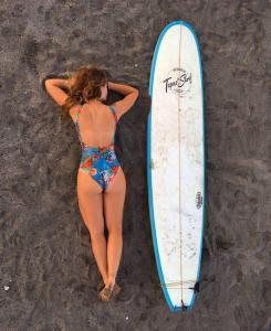 una mujer acostada en la playa junto a una tabla de surf en Tapas & Surf, en Petacaltepe
