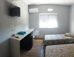 Habitación con 2 camas, escritorio y TV. en Hotel Majestic, en Pelotas