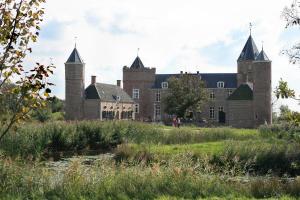 an old castle with two towers and a pond at Bed & Breakfast Zeeduinsepoort met Sauna in Oostkapelle