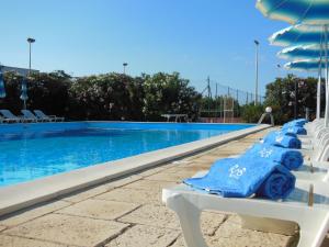 a swimming pool with white chairs and blue towels at Residence Club Barbara in Ostuni