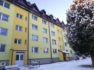 a yellow building with snow in front of it at Apartman May Tatranska Lomnica in Tatranská Lomnica