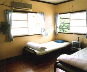 a small room with a bed and two windows at Minshuku Rakutenya in Ishigaki Island