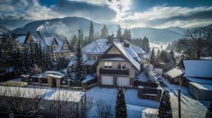 a house is covered in snow with trees and mountains at Rezydencja Marjo z basenem in Kościelisko