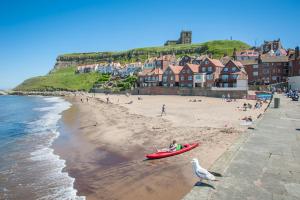 a beach with people and a red boat on it at Lobster Hall - Room Only in Whitby