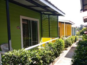 三克拉布里的住宿－Sripech Home，绿色的房子,设有黄色和绿色的窗户和灌木丛