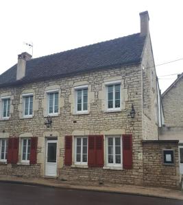 un antiguo edificio de piedra con persianas rojas en una calle en Chambres d'hôtes la Chaumière en Arcy-sur-Cure